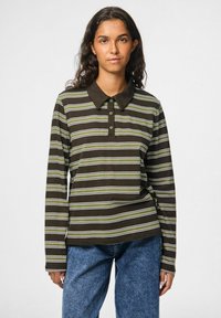 Bruine lange mouwen polo shirt met groene en witte horizontale strepen, voorzien van een knoopsluiting en een donkere kraag, gecombineerd met blauwe spijkerbroek.