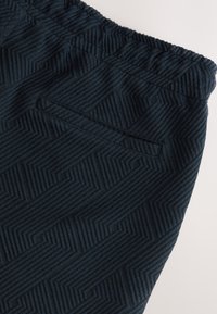 Dark blue shorts featuring a textured geometric pattern, elastic waistband, and a rear pocket for functionality.