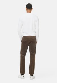 Brune kordfløjele bukser med lige ben-design. Bæres med en langærmet hvid skjorte og hvide sneakers. Bagudsigt der viser lommer.