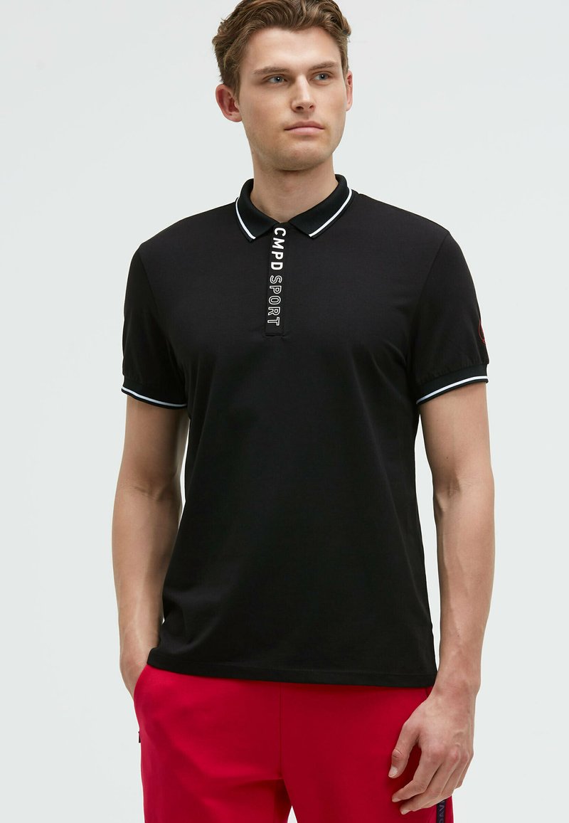 Camisa polo negra con collar, con acentos blancos en el collar y las mangas. Detalle central del logo que dice "CMPD SPORT". Textura suave.