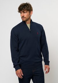 Marineblauer Pullover mit einem Viertel-Reißverschlusskragen, gerippten Bündchen und Saum, der ein kleines rotes Logo auf der Brust trägt. Hergestellt aus einem strukturierten Strickstoff.
