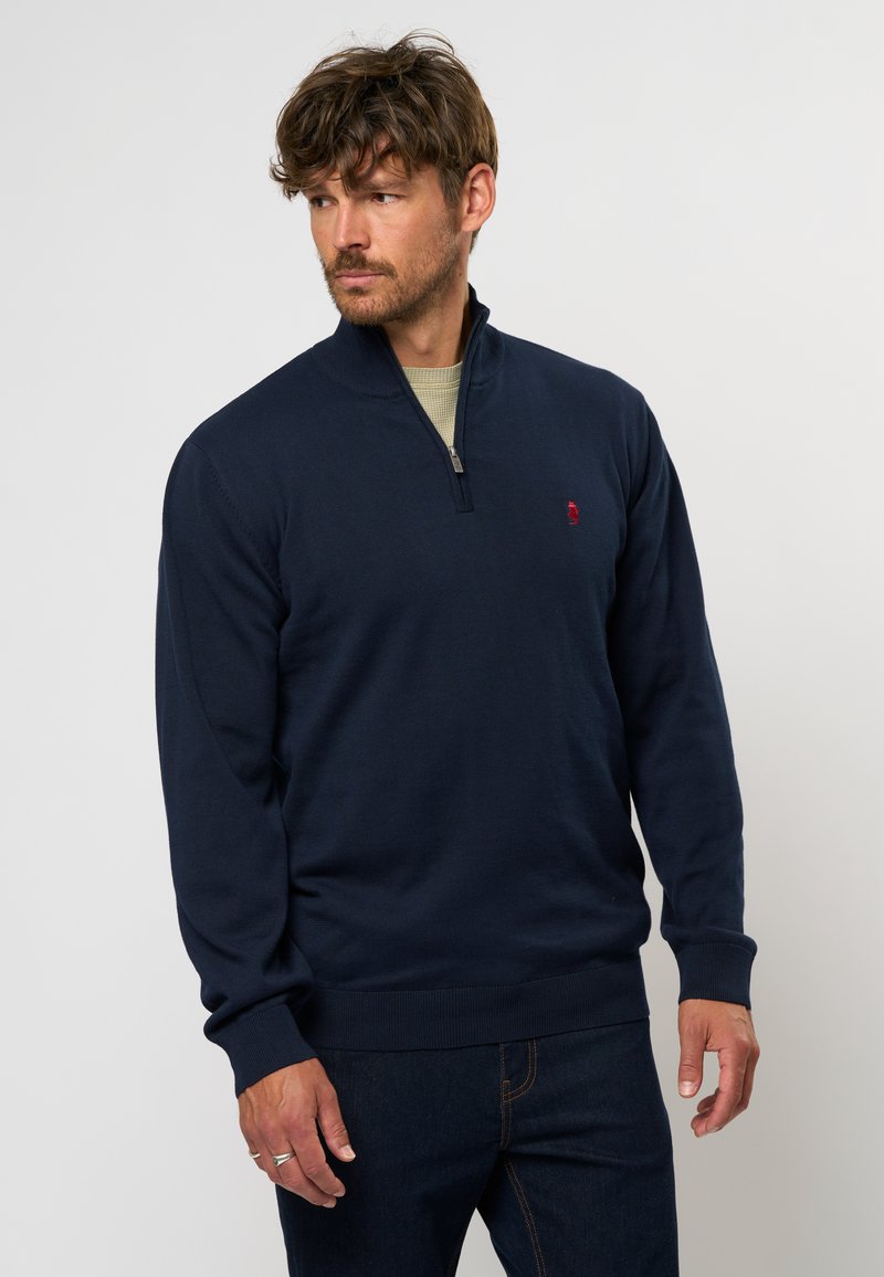 Tumed sinine pullover neljandiku tõmbluku kraega, ribadega mansetid ja äär, millel on rinna peal väike punane logo. Valmistatud tekstureeritud kudumiskangast.