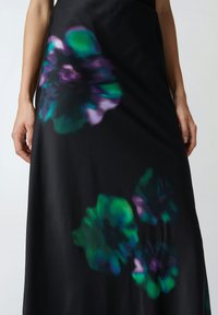 Jupe noire avec de grands motifs floraux abstraits dans des teintes de vert et de violet. Texture lisse avec une silhouette fluide.