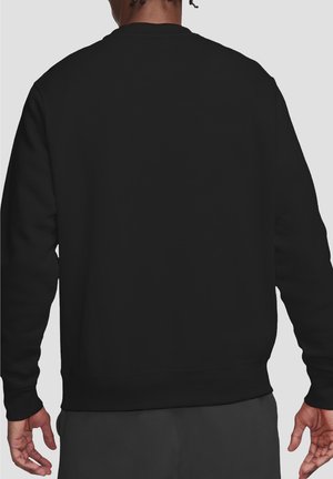 Man wearing plain black long-sleeve shirt and dark pants, shown from the back against a neutral background.