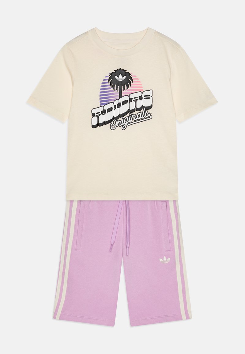 Krema majica s crnim logotipom "Adidas Originals" i grafikom palme, u kombinaciji s ljubičastim šortsem s bijelim bočnim trakama i Adidas logom.