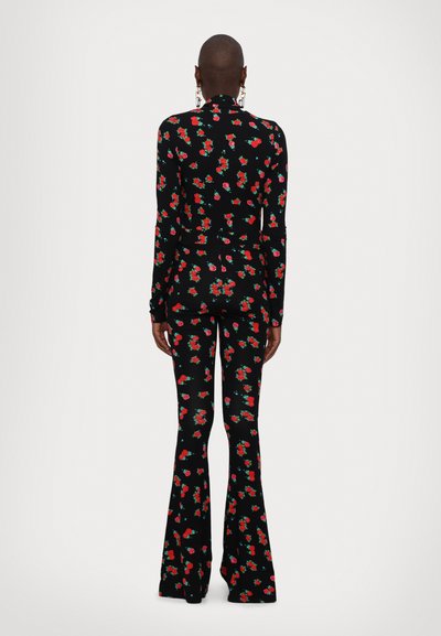 Combinaison florale à manches longues, avec une couleur de base noire, un motif de roses rouges et vertes, et des jambes de pantalon évasées. Tissu lisse et extensible.