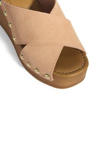 Roze suède wedge sandaal met gekruiste banden, voorzien van goudkleurige studs en een bruine platform met stiksel op de voetbed.