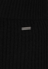 Czarna dzianinowa czapka beanie z prążkowaną teksturą i małą srebrną metką z napisem "DREIMASTER" przymocowaną z przodu.