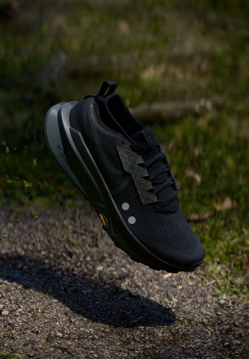 Zapatilla deportiva negra hecha de material sintético, con una parte superior transpirable, patrones texturizados y una suela acolchada con una suela con patrón.