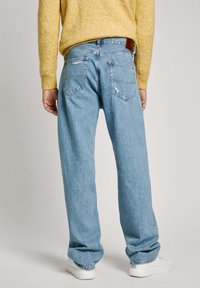 Svijetloplave traperice s opuštenim krojem, koje imaju stražnje džepove, lagano izblijedjenje i smeđu kožnu oznaku na pojasu.