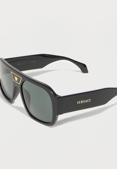 Μαύρα ορθογώνια γυαλιά ηλίου Versace με σκοτεινούς φακούς, χρυσό έμβλημα Μέδουσας στη γωνία και λογότυπο Versace στο μπράτσο.