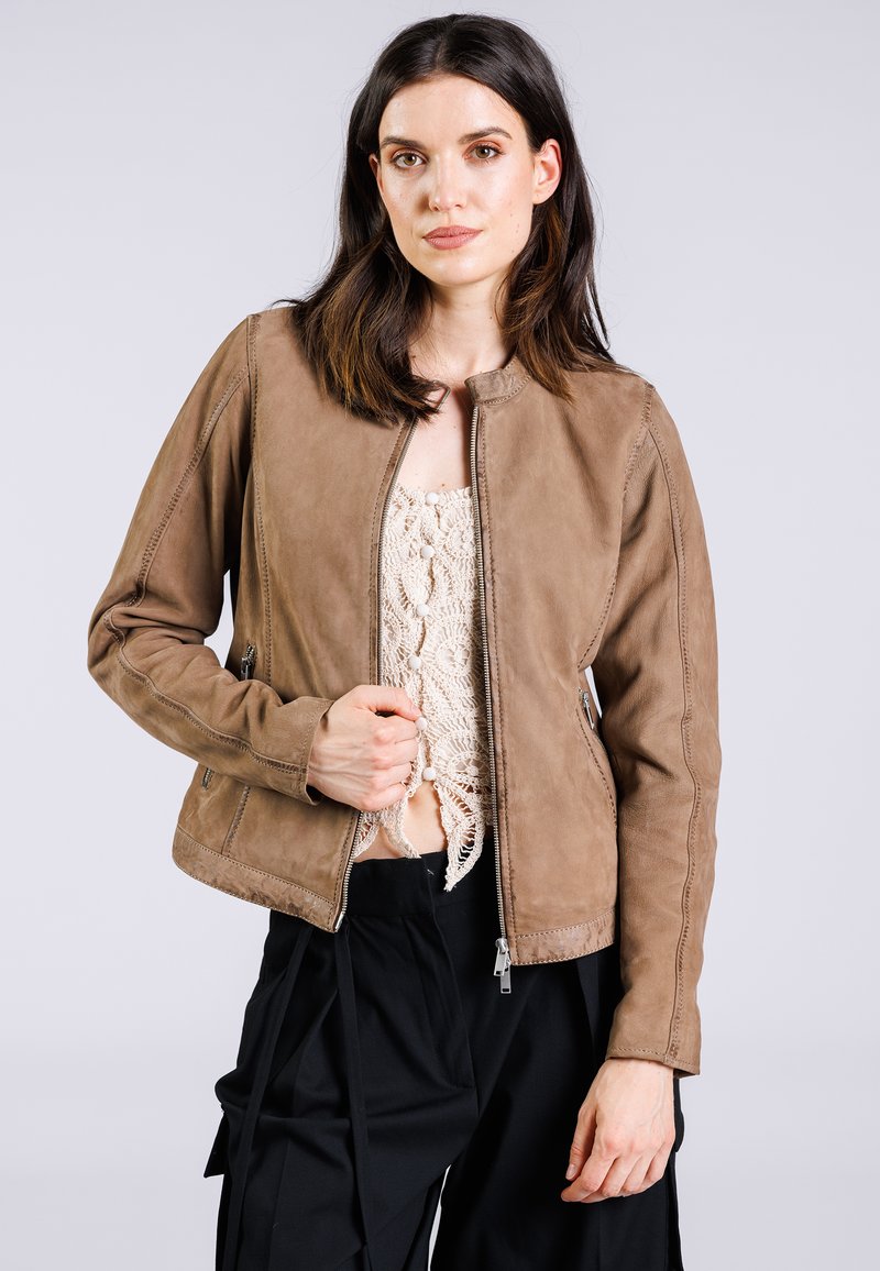 Giacca in pelle marrone con scollatura rotonda, chiusura con cerniera, tasche laterali e dettagli sulle cuciture, indossata sopra un leggero top all'uncinetto.