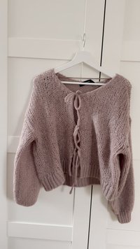 Ljus mauve stickad cardigan med rund halsringning, långa ärmar och knytstängning framtill med ribbade muddar och fåll.