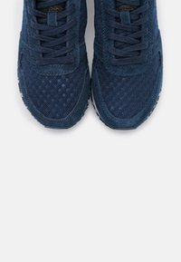 Baskets bleu marine en mesh et daim, avec bout rond, lacets plats et semelle extérieure en caoutchouc blanc ; détail de la surface supérieure texturée visible.