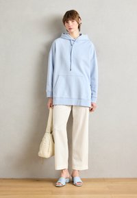 Felpa oversize azzurro chiaro con tasca frontale, abbinata a pantaloni a gamba larga in corduroy color crema e sandali a scivolo azzurro chiaro. Trame dei tessuti casual.