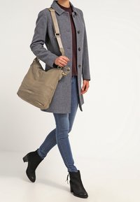 Grå ullkappa, vinröd topp, blå jeans och svarta ankelstövlar. Bär en mjuk taupe axelväska med avtagbar rem och metalldetaljer.