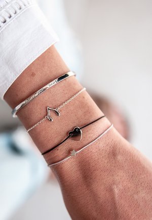 Četiri narukvice na zapešću: srebrni bangle ugraviran "Slijedi svoje srce", srebrni šećerasti ukras u obliku kosti sreće, crni srčasti ukras i srebrni ukras u obliku zvijezde.