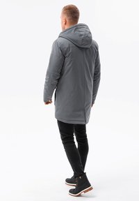 Grå utomhusjacka med huva, lång design och synliga sömmar. Bärs med svarta jeans och ankelboots med bruna sulor.