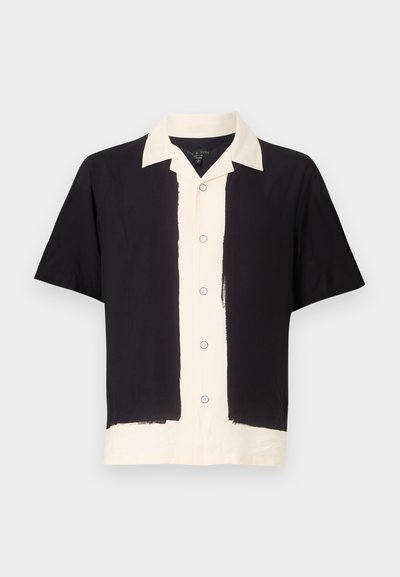 Camisa de manga corta en negro y crema. Presenta un lado izquierdo negro, un lado derecho crema con un cierre de botones y un cuello en contraste. Fabricada en una tela suave.