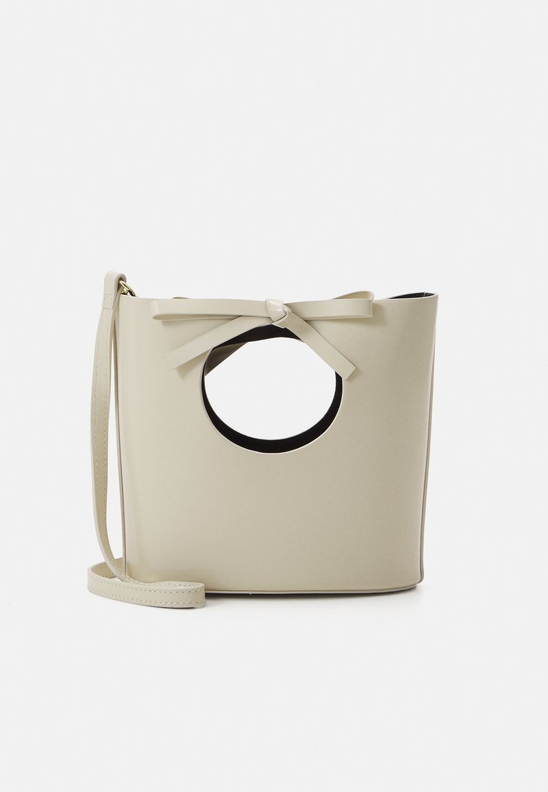Μπεζ, λείο τσάντα από τεχνητό δέρμα με στρογγυλή κοπή στη λαβή, λεπτομέρεια φιόγκου στην κορυφή και ρυθμιζόμενο λουρί, που διαθέτει μινιμαλιστικό σχέδιο.