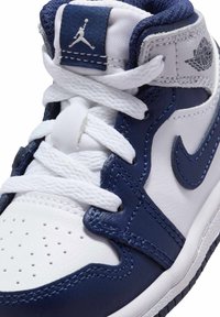 Sneaker in pelle bianca e navy con design high-top, lacci bianchi, punta perforata e branding Air Jordan sulla linguetta e sul lato.