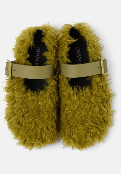 Fuzzy olive green clogs with a soft, shaggy texture. Features beige adjustable buckle straps and a black insole. Rounded silhouette.