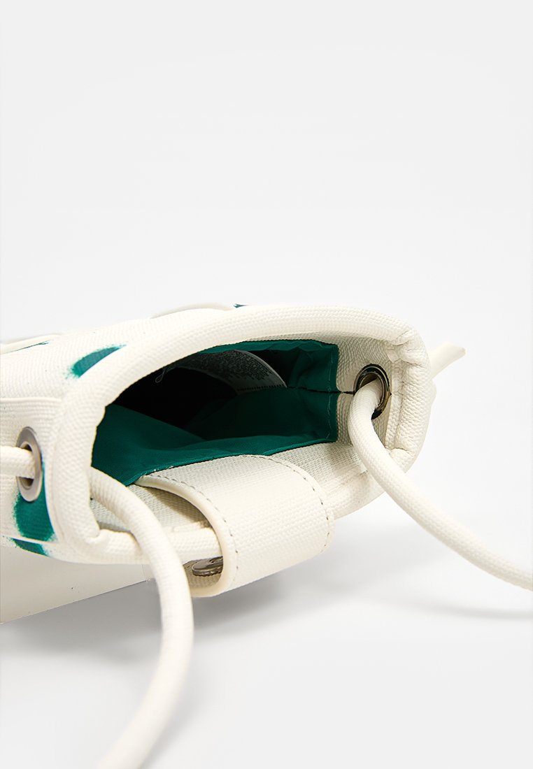 Witte canvas trekkoord tas met groene binnenvoering, opengebeeld en benadrukt de metalen oogjes en stoffen schouderriem op een effen witte achtergrond.