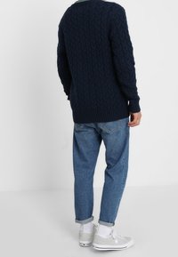 Marinblå stickad tröja med ett texturerat kabelmönster, ribbade muddar, i kombination med ljusblå uppvikta jeans och grå sneakers.