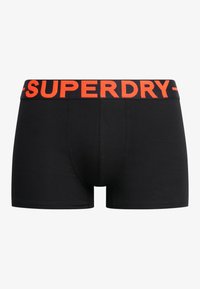 Schwarze Boxershorts mit einem orangen elastischen Bund, auf dem das "SUPERDRY"-Logo steht. Glattes Material, enganliegendes Design und Oberschenkellänge.