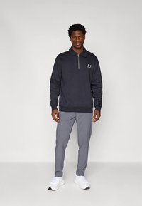 Tengerészkék, negyedcipzáras pulóver bordázott mandzsettákkal és szegéllyel, apró logóval az oldalon, világosszürke, szűk szárú nadrággal és fehér tornacipővel párosítva.