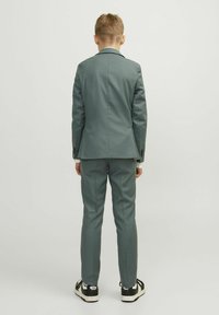 Veste et pantalon de costume gris à coupe ajustée, associés à des baskets noir et blanc. Tissu lisse avec une texture subtile et aucun motif visible.