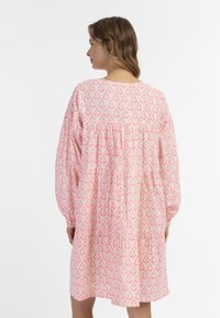 Ružové šaty s vzorom a dlhými rukávmi, s nariaseným živôtikom a voľným áčkovým strihom. Obsahujú kvetinový dizajn v tmavších ružových odtieňoch.