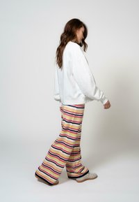 Fehér, oversized pulóver bordás mandzsettákkal, bőszárú, színes csíkos nadrággal párosítva, amely vízszintes mintázatban pink, sárga és fekete színeket tartalmaz.