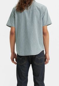 Koszula z krótkim rękawem w jasnoniebieskie i białe paski, z zaokrąglonym dołem i luźnym krojem, skomponowana z ciemnoniebieskimi dżinsami.