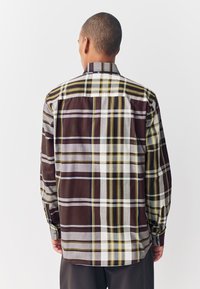 Camicia a maniche lunghe a quadri con una combinazione di quadrati marroni, bianchi e gialli, polsini con bottoni e orlo dritto sul retro.