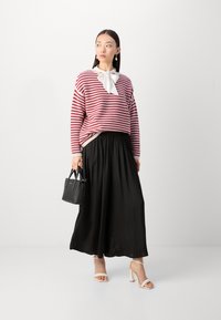 Röd och vit randig tröja med en vit rosett, parat med en lång svart plisserad kjol. Accessoarer inkluderar en liten svart handväska och nakenfärgade klackar.