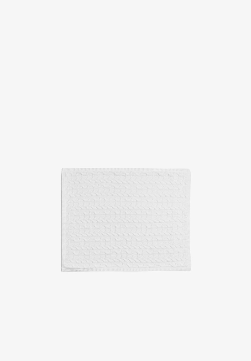 Tapis de bain en coton blanc avec un motif à côtes texturé et des bords tissés, de forme rectangulaire et avec une surface douce. Dimensions non spécifiées.