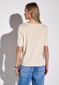 Maglione beige a maniche corte con una vestibilità morbida, scollo rotondo e texture morbida. Indossato con jeans in denim azzurri. Design semplice e minimal.