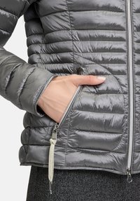 Grijze pufferjack met horizontale quilting, een zijritszak en een gestructureerd oppervlak. Subtiele glans en lichtgewicht ontwerp.