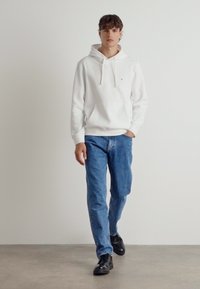 Weiße Kapuzen sweatshirt mit Kängurutasche und Zugbändern. Kombiniert mit hellblauen Jeans und schwarzen Schuhen. Einfaches, lässiges Design.