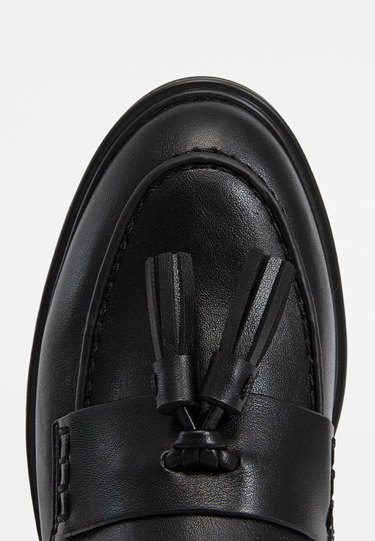 Mocassini in pelle nera con finitura liscia, nappine decorative e punta arrotondata. La suola presenta un bordo sollevato discreto.