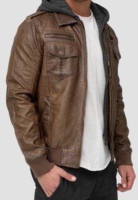 Chaqueta de cuero marrón con un acabado texturizado, bolsillos con cremallera y una sudadera gris debajo, con puños y cintura acanalados.
