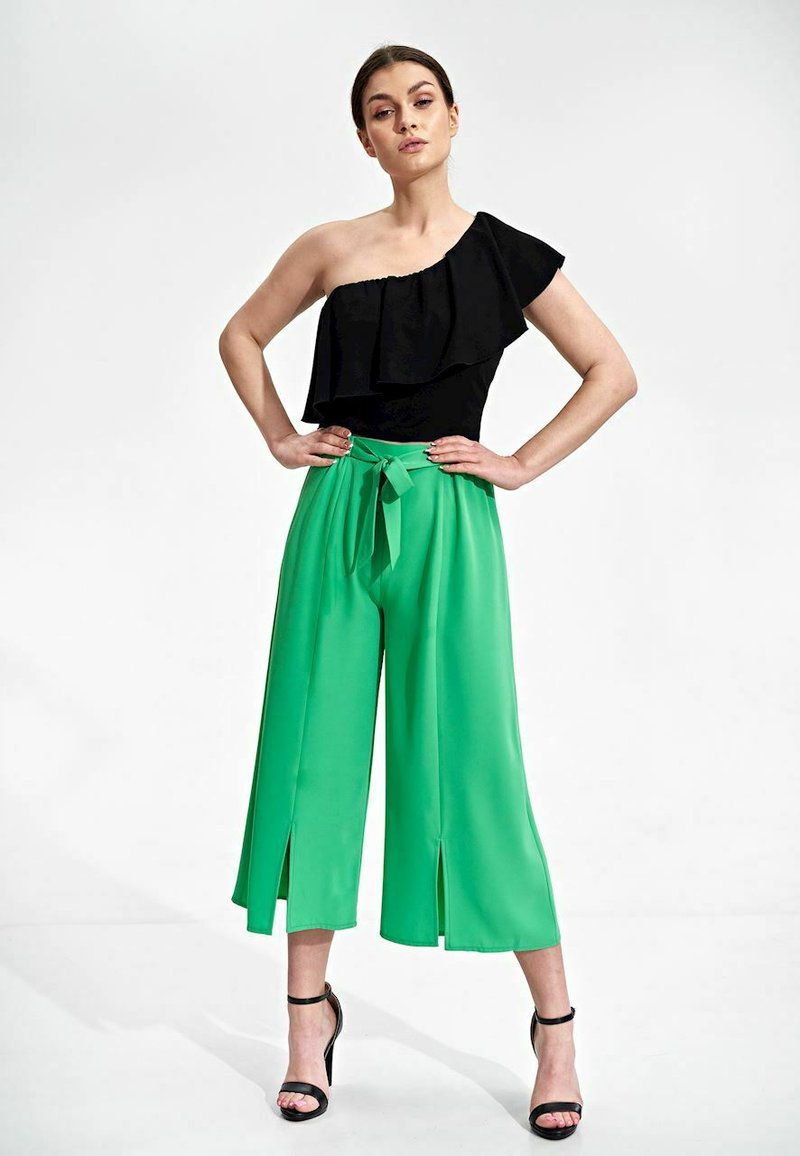 Czarny top na jedno ramię z falbanami, w połączeniu z wysokimi, zielonymi spodniami o szerokich nogawkach z bocznymi rozcięciami i wiązanym paskiem w talii.