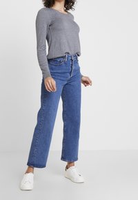 Grå langærmet top, højtaljede blå straight-leg jeans og hvide sneakers med en diskret leopardaccent på hælen. Enkel design.
