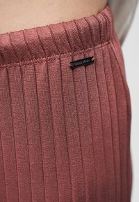 Κοντινή λήψη ριμπ πλεκτού υφάσματος σε ροζ χρώμα με μια μικρή μαύρη ετικέτα Calvin Klein ραμμένη κοντά στην κορυφή.