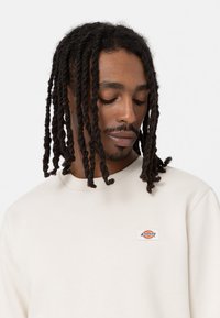 Crème sweatshirt van katoenmix, met een geribbelde ronde hals en een klein geborduurd logo op de linkerkant van de borst.