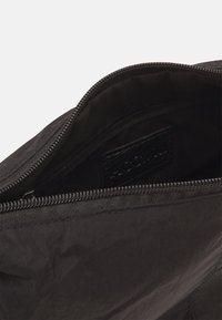 Schwarze Stofftasche mit Reißverschluss, mit glatter Oberfläche und einer kleinen Innentasche, die mit einem Logo versehen ist.
