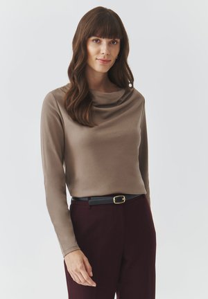Top beige de manga larga con escote drapeado, hecho de una tela suave, combinado con pantalones burdeos oscuros y un cinturón negro con hebilla dorada.