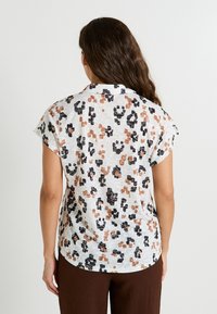 Chemise à manches courtes et col, en tissu léger, avec un fond blanc et un motif animalier noir et brun. Texture lisse.