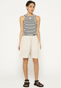 Canottiera a righe in bianco e nero, abbinata a pantaloni shorts beige con vita elastica. Il modello indossa sandali neri con cinturini.